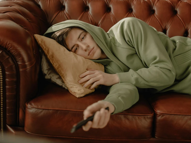 a person laying on a couch with a remote, trending on pexels, hyperrealism, wearing green jacket, looking tired, asian male, wearing a grey hooded sweatshirt