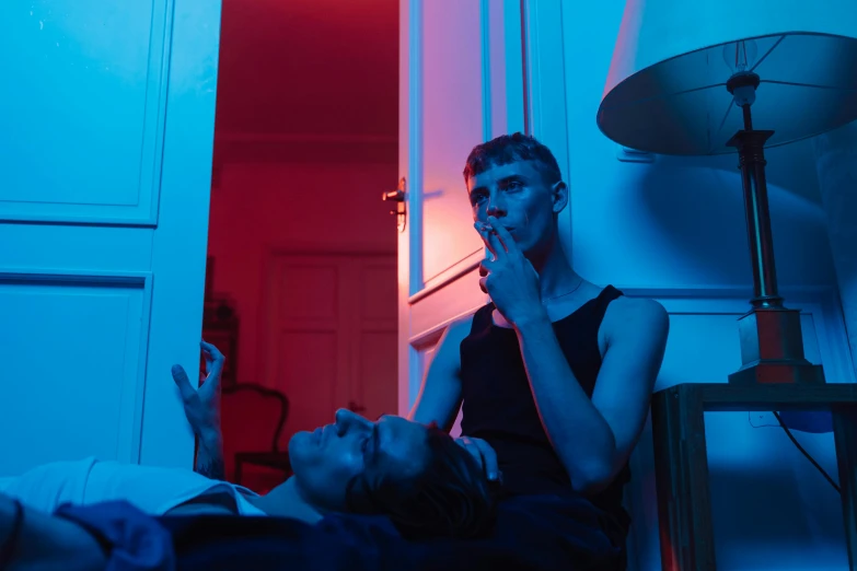 a man sitting on top of a bed next to a woman, inspired by Nan Goldin, pexels contest winner, bauhaus, blue and red lights, they are smoking, two young men, petra collins and mc. escher