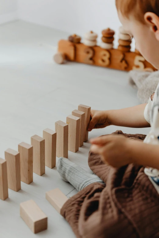 a little boy sitting on the floor playing with wooden blocks, pexels contest winner, natural muted tones, closeup of arms, contaning tables and walls, product introduction photo