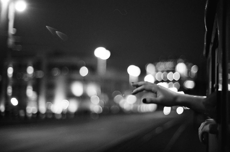 a person reaching out of a train window at night, a black and white photo, by Daniel Gelon, city lights bokeh, cinematic. by leng jun, olga buzova, finger