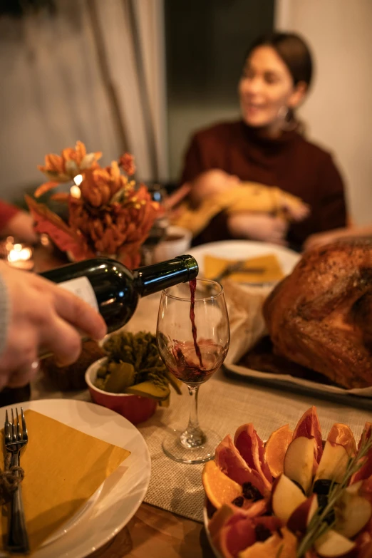 a group of people sitting around a table filled with food, with a bottle of wine, turkey, profile image, up close
