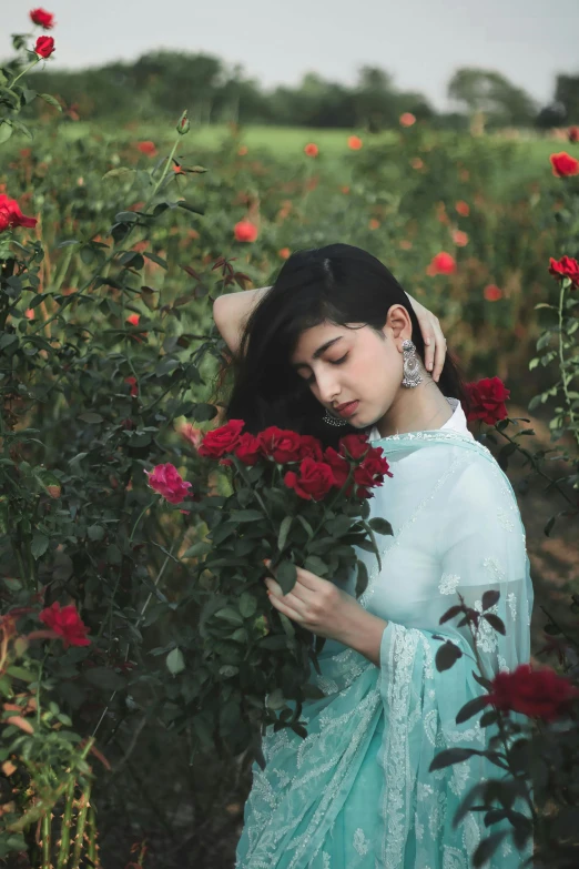 a woman standing in a field of red roses, inspired by Elsa Bleda, pexels contest winner, assamese aesthetic, handsome girl, islamic, teal aesthetic