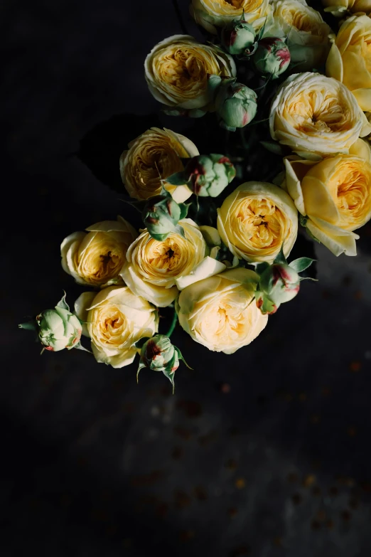 a bunch of yellow roses sitting on top of a table, inspired by François Boquet, unsplash, baroque, dark backdrop, bottom body close up, soft white glow, a high angle shot