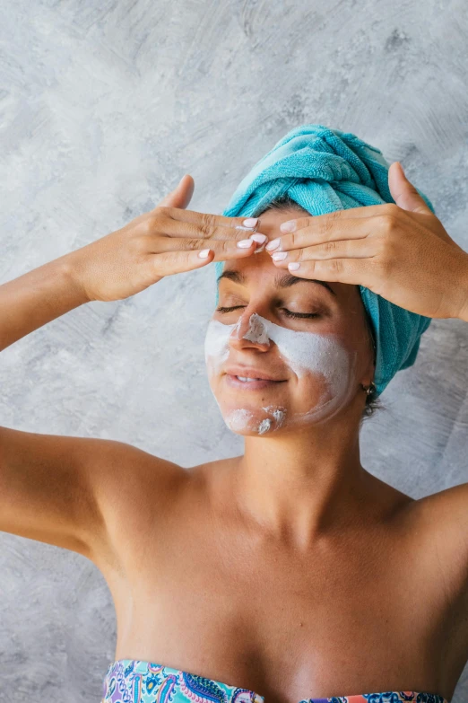 a woman with a towel on her head and a towel on her head, mask off, hands on face, blending, looking happy