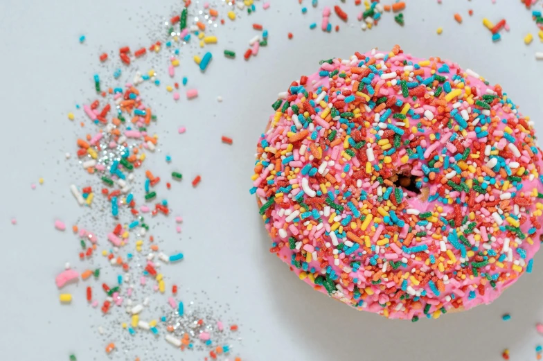 a sprinkled donut sitting on top of a white surface, trending on unsplash, brightly coloured, brightly-lit, cakes, adafruit