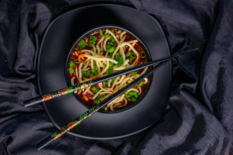 a black plate topped with noodles and chopsticks, inspired by Tan Ting-pho, pexels contest winner, dau-al-set, alphabet soup, high resolution product photo, brilliantly coloured, spicy