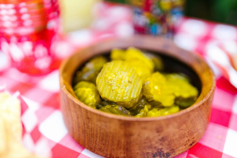 a wooden bowl filled with pickles on top of a table, by Julia Pishtar, yellow, moroccan, picnic, puerto rico