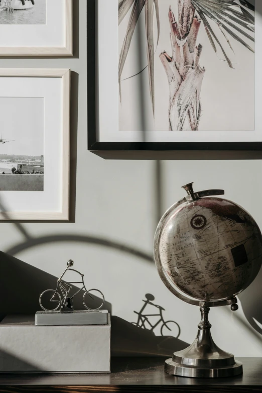 a globe sitting on top of a wooden table, poster art, inspired by Willem Claeszoon Heda, pexels contest winner, visual art, bicycle in background, picture frames, charcoal and silver color scheme, photos of family on wall
