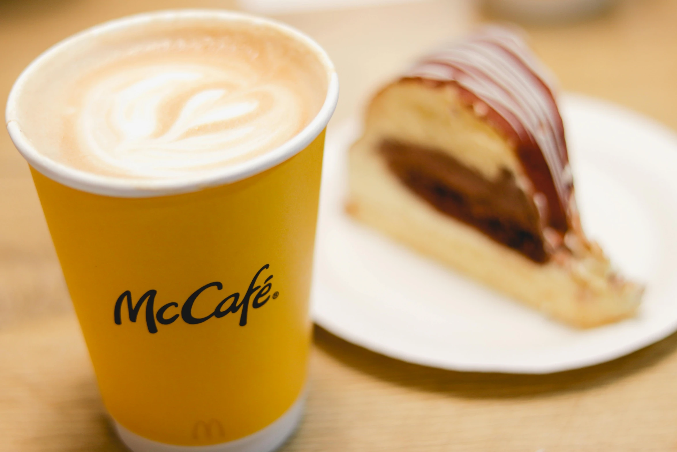 a piece of cake on a plate next to a cup of coffee, by Peter McArdle, mcdonalds interior background, macguire is a tall, thumbnail, profile image