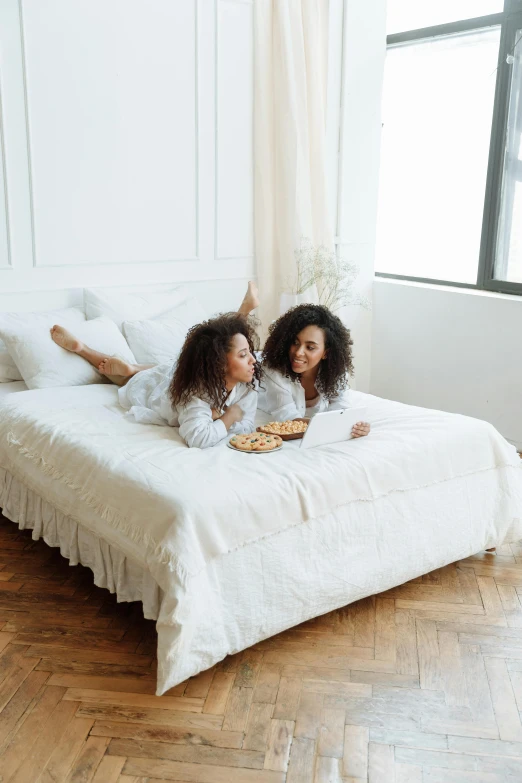 a couple of women laying on top of a bed, snacks, all white, very comfy, premium quality