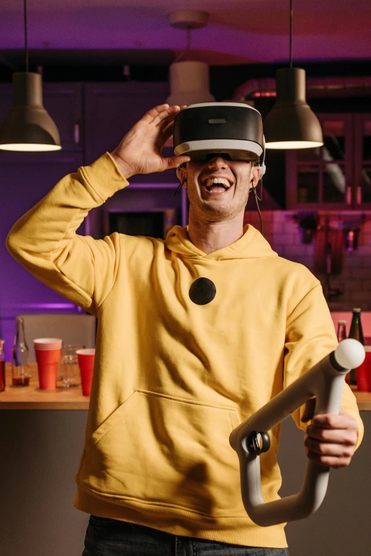 a man in a yellow hoodie holding a video game controller, a hologram, by Matthias Stom, pexels, happening, standing in a cantina, vr iridium visor, head bent back in laughter, college