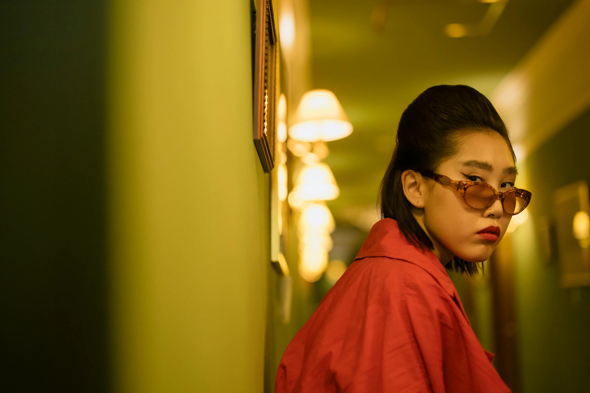 a woman with glasses leaning against a wall, an album cover, inspired by Elsa Bleda, trending on pexels, photorealism, 8 0 s asian neon movie still, hotel room, wearing red and yellow clothes, chinese empress