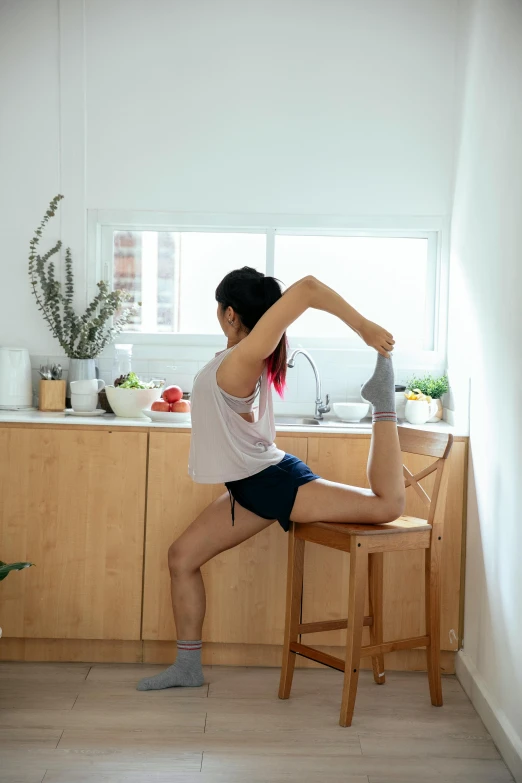 a woman sitting on top of a wooden chair in a kitchen, by Jang Seung-eop, pexels contest winner, arabesque, dynamic stretching, lower body, arched back, thigh focus