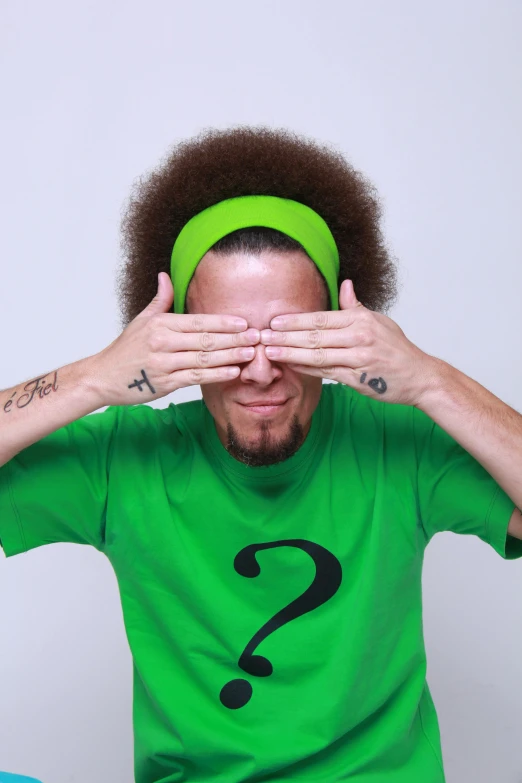 a man with a green shirt covering his eyes, an album cover, inspired by Jeremy Henderson, pexels, big afro, neymar jr, wide eyed, in 2 0 1 2