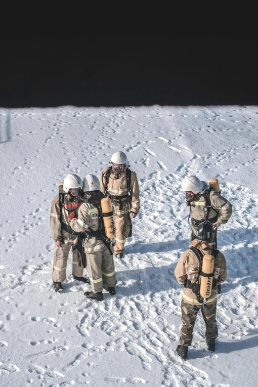 a group of men standing on top of a snow covered slope, firefighting gear, wide overhead shot, tan, training