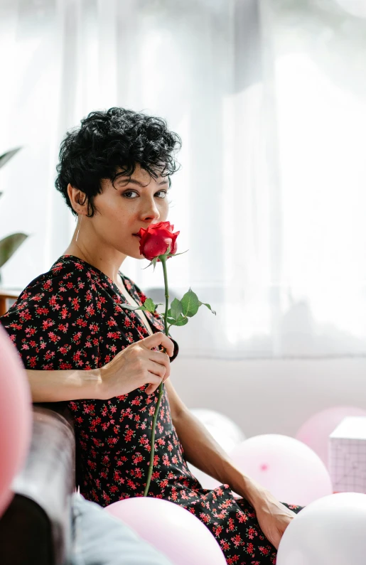 a woman sitting on a bed holding a rose, by Winona Nelson, pexels, short black pixie cut hair, sarah andersen, giant carnation flower head, andrew gonzalez