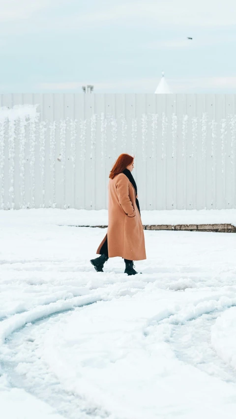 a woman walking across a snow covered field, inspired by Louisa Matthíasdóttir, pexels contest winner, visual art, ( redhead, exiting store, long coat, helsinki