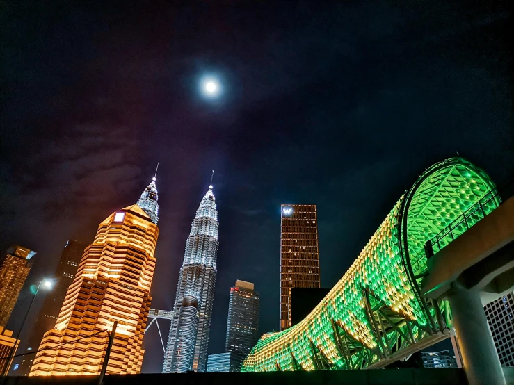 a view of a city at night with a full moon in the sky, by Bernardino Mei, pexels contest winner, hurufiyya, malaysian, tall structures, lit from below, coloured photo