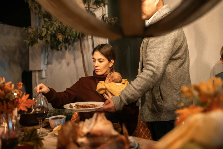 a woman holding a baby at a dinner table, pexels contest winner, renaissance, wine cellar full of food, husband wife and son, gif, lachlan bailey