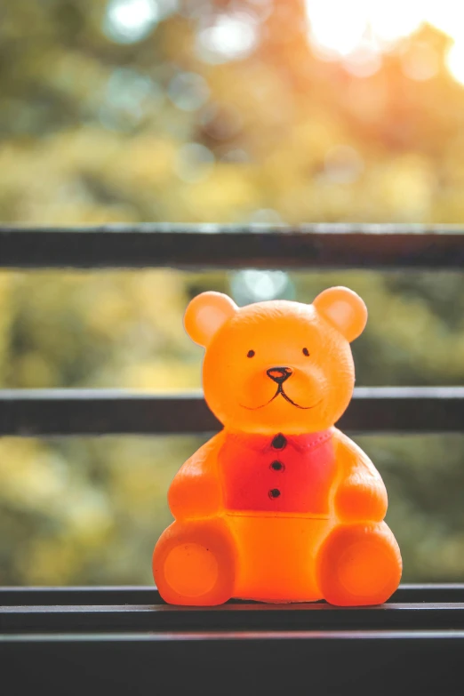 a close up of a toy bear on a bench, a cartoon, unsplash, orange yellow, sitting on a window sill, plastic toy, standing