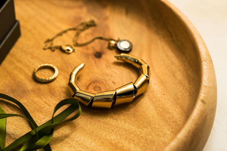 a gold bracelet sitting on top of a wooden tray, a still life, by Julia Pishtar, unsplash, metal neck rings, bamboo, product display photograph, upcycled