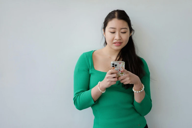 a woman is looking at her cell phone, inspired by helen huang, realism, wearing green, instagram photo shoot, south east asian with long, student