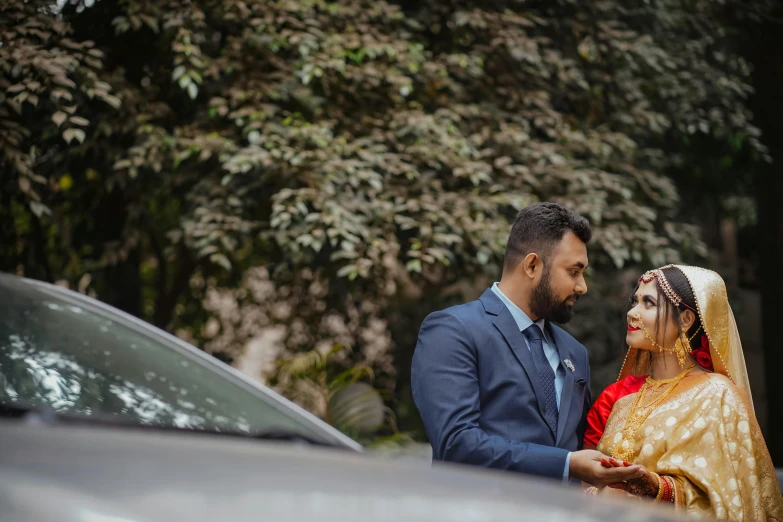 a man and woman standing next to each other in front of a car, by Max Dauthendey, pexels contest winner, hurufiyya, assamese aesthetic, bride and groom, wide screenshot, looking from side