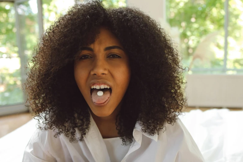 a woman sticking her tongue out while sitting on a bed, by Lily Delissa Joseph, pexels contest winner, barbecuing chewing gum, with curls, wearing a white button up shirt, zenra taliyah