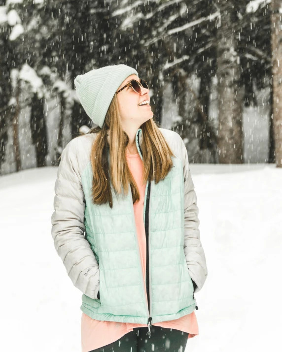 a woman standing in the snow with her eyes closed, a colorized photo, pexels contest winner, seafoam green, laughing, grey jacket, trending on vsco