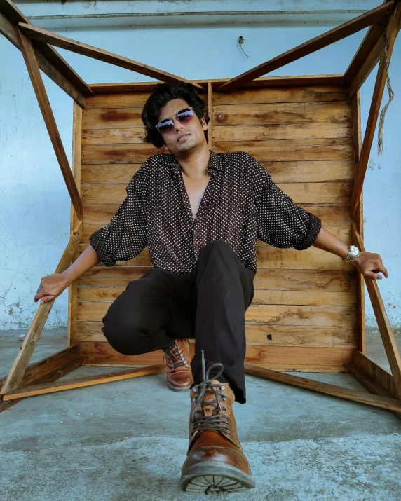 a man sitting on top of a wooden box, an album cover, by Byron Galvez, unsplash, op art, wears brown boots, assamese aesthetic, wearing shades, androgynous person