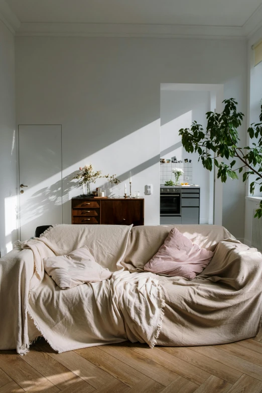 a living room with a couch covered in a blanket, unsplash contest winner, light and space, sunlight filtering through skin, pale colors, lpoty, late summer evening