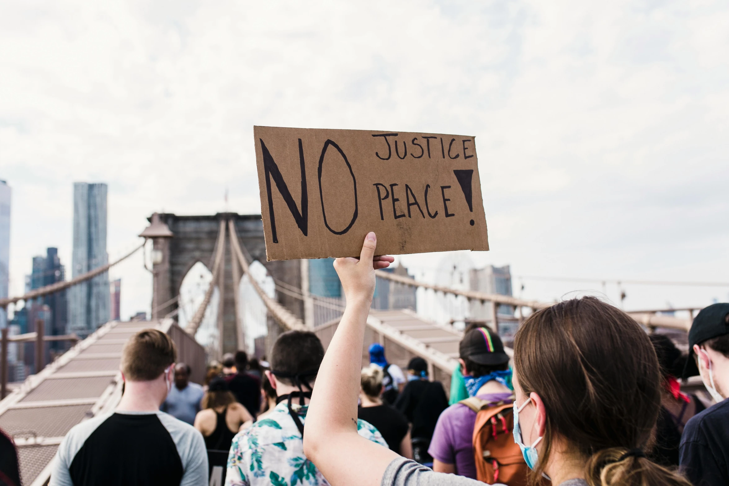 a woman holding a sign that says no justice peace, by Julia Pishtar, pexels, attacking nyc, instagram post, brown, 2000s photo