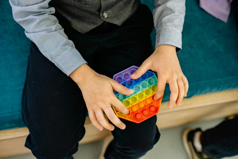 a person sitting on a couch holding a toy, inspired by Ernő Rubik, pexels, interactive art, rainbow bubbles, school class, made of rubber, hexagonal shaped