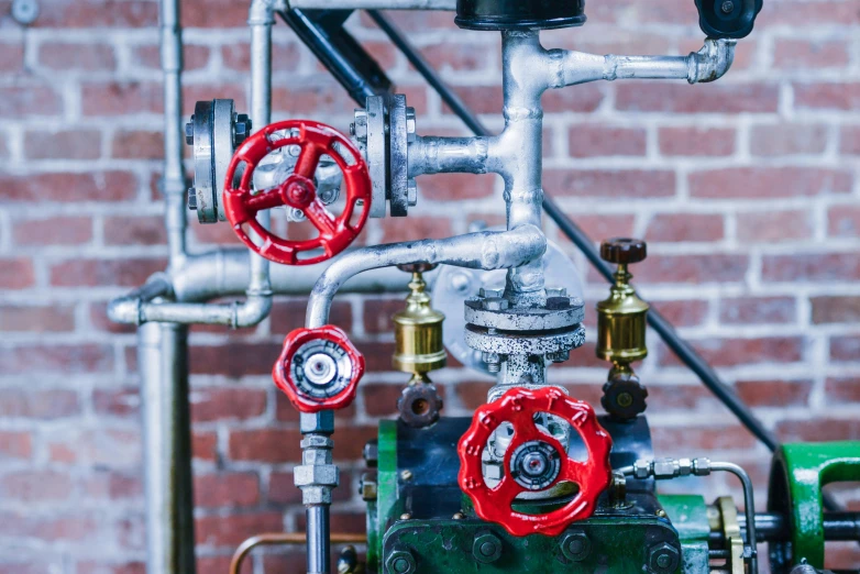 a green and red fire hydrant next to a brick wall, by Daniel Lieske, pexels contest winner, with gears and tubes, glass pipes showing red, steel plating, worksafe. instagram photo