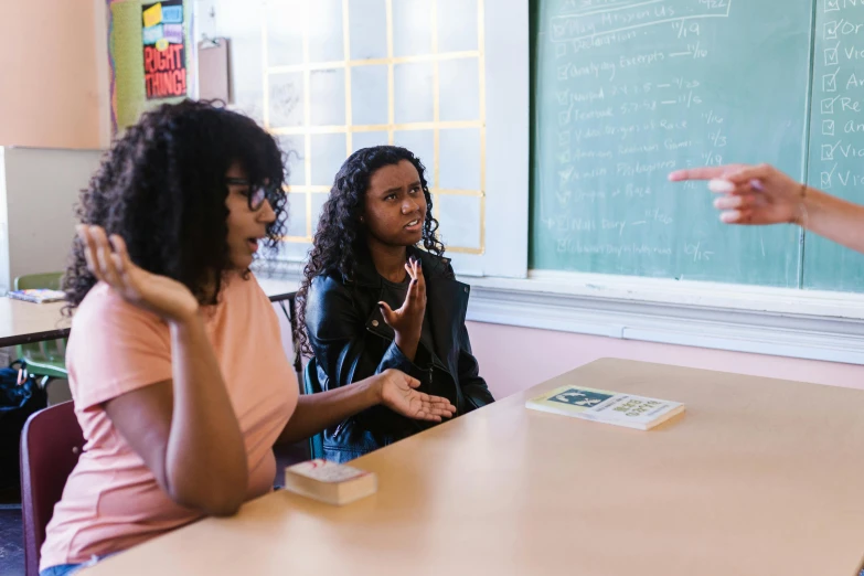 a group of people sitting at a table in front of a blackboard, aida muluneh, scolding, alexis franklin, classroom background