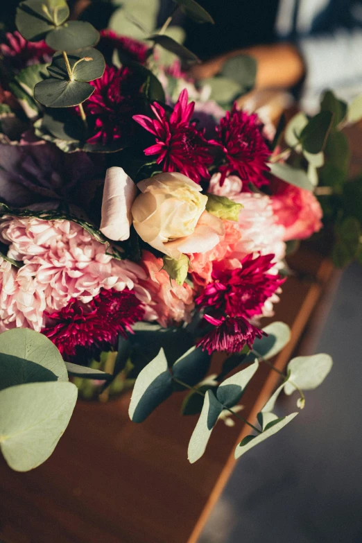 a bouquet of flowers sitting on top of a wooden table, pink and red color scheme, upclose, loosely cropped, carefully crafted