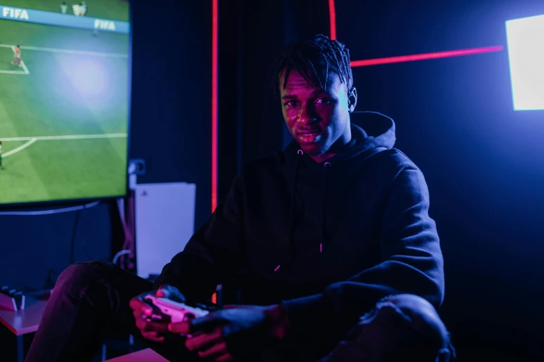 a man sitting in front of a tv playing a video game, pexels contest winner, playboi carti portrait, soccer, with neon lights, ( ( dark skin ) )