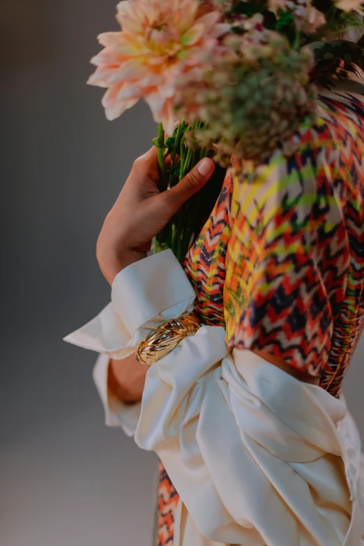 a woman holding a bunch of flowers in her hands, an album cover, inspired by Anna Füssli, trending on pexels, intricate silk clothing, colourful close up shot, hands pressed together in bow, extravagant feathered collar