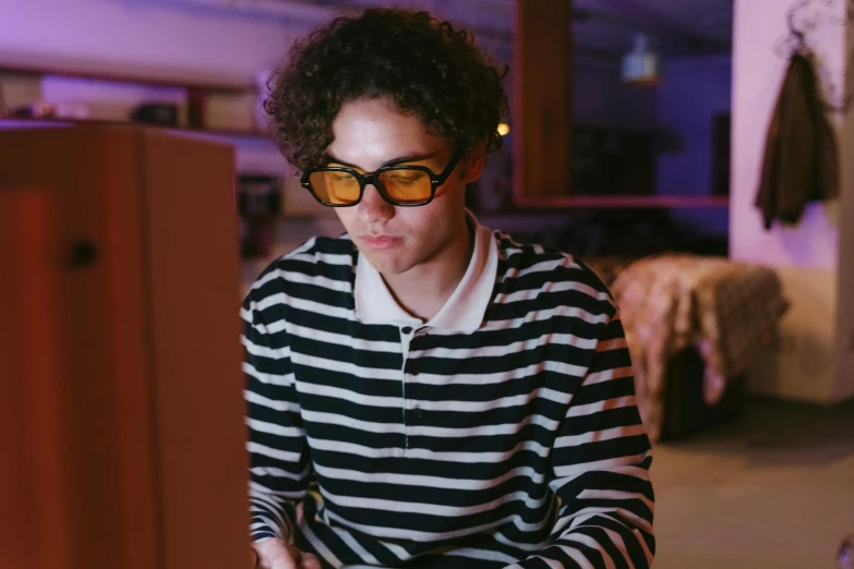 a man sitting in front of a laptop computer, pexels, computer art, finn wolfhard, yellow carrera glasses, striped, low lighting