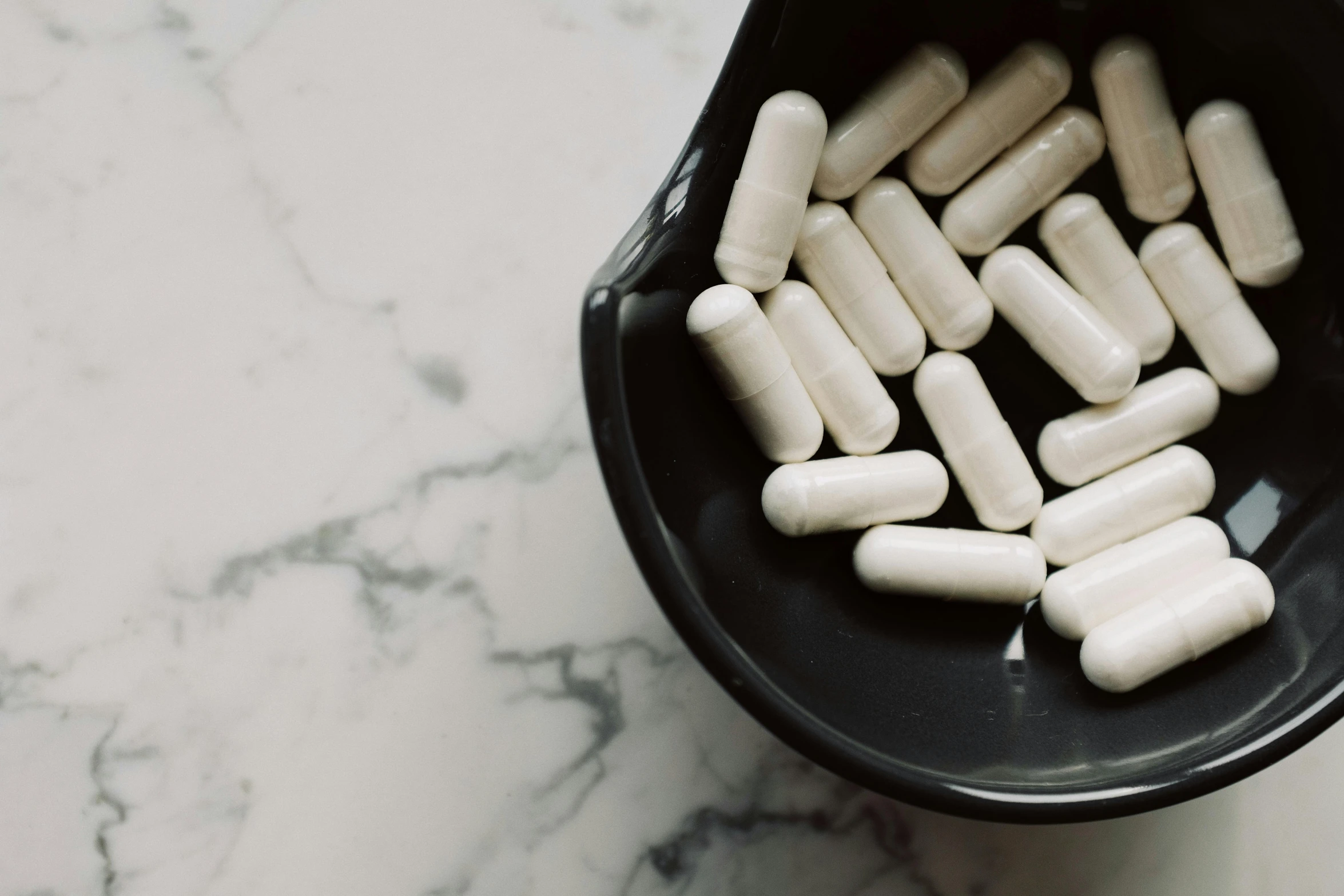 a black bowl filled with white pills on top of a marble counter, by Emma Andijewska, unsplash, antipodeans, alien capsules, white sleeves, instagram post, shot on sony a 7