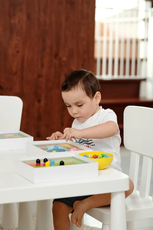 a little boy that is sitting at a table, board games on a table, pastel artwork, activity play centre, on wooden table