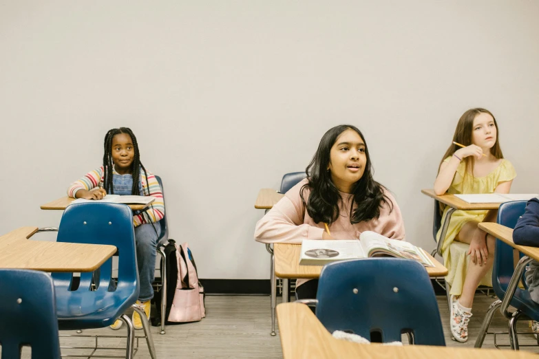 a group of children sitting at desks in a classroom, a portrait, by Carey Morris, trending on unsplash, fan favorite, high school girls, looking sideways, high quality photo
