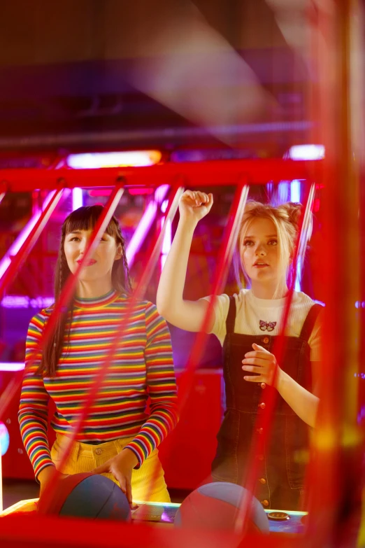 a couple of women standing next to each other, an album cover, by Julia Pishtar, pexels, kitsch movement, arcade game, ginger, behind bars, red lasers