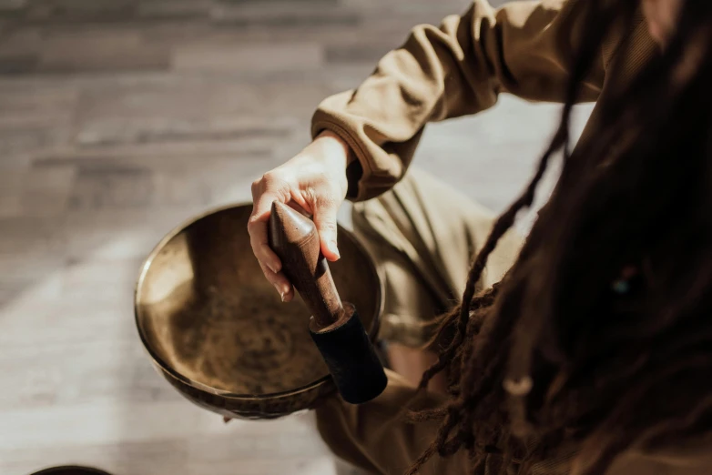 a person with dreadlocks playing a musical instrument, by Julia Pishtar, trending on pexels, bowl, figure meditating close shot, holding a bell, brown