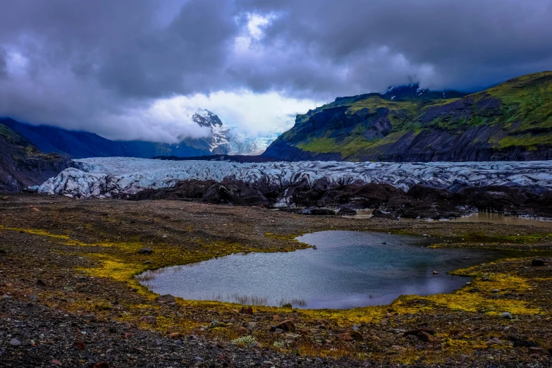 a body of water with a mountain in the background, inspired by Þórarinn B. Þorláksson, pexels contest winner, glaciers, dramatic earth colors, low clouds after rain, ground - level medium shot