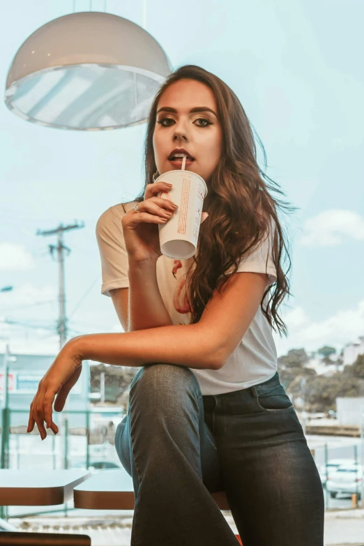 a woman sitting at a table with a drink in her hand, trending on pexels, photorealism, soft devil queen madison beer, confident action pose, aussie baristas, summer day