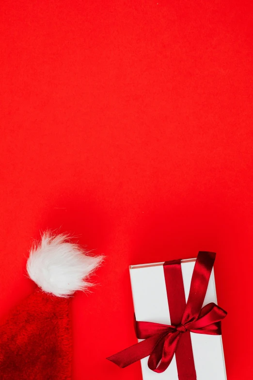 a santa hat and a gift on a red background, by Julia Pishtar, pexels contest winner, with white fluffy fur, square, demur, overview