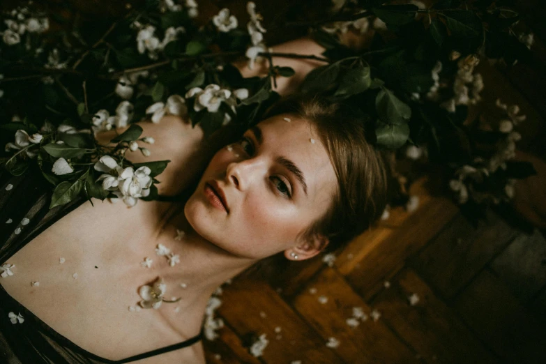 a woman laying on top of a wooden floor covered in flowers, a picture, inspired by Elsa Bleda, trending on pexels, beautiful delicate face, ewa juszkiewicz, vintage photo, branches sprouting from her head