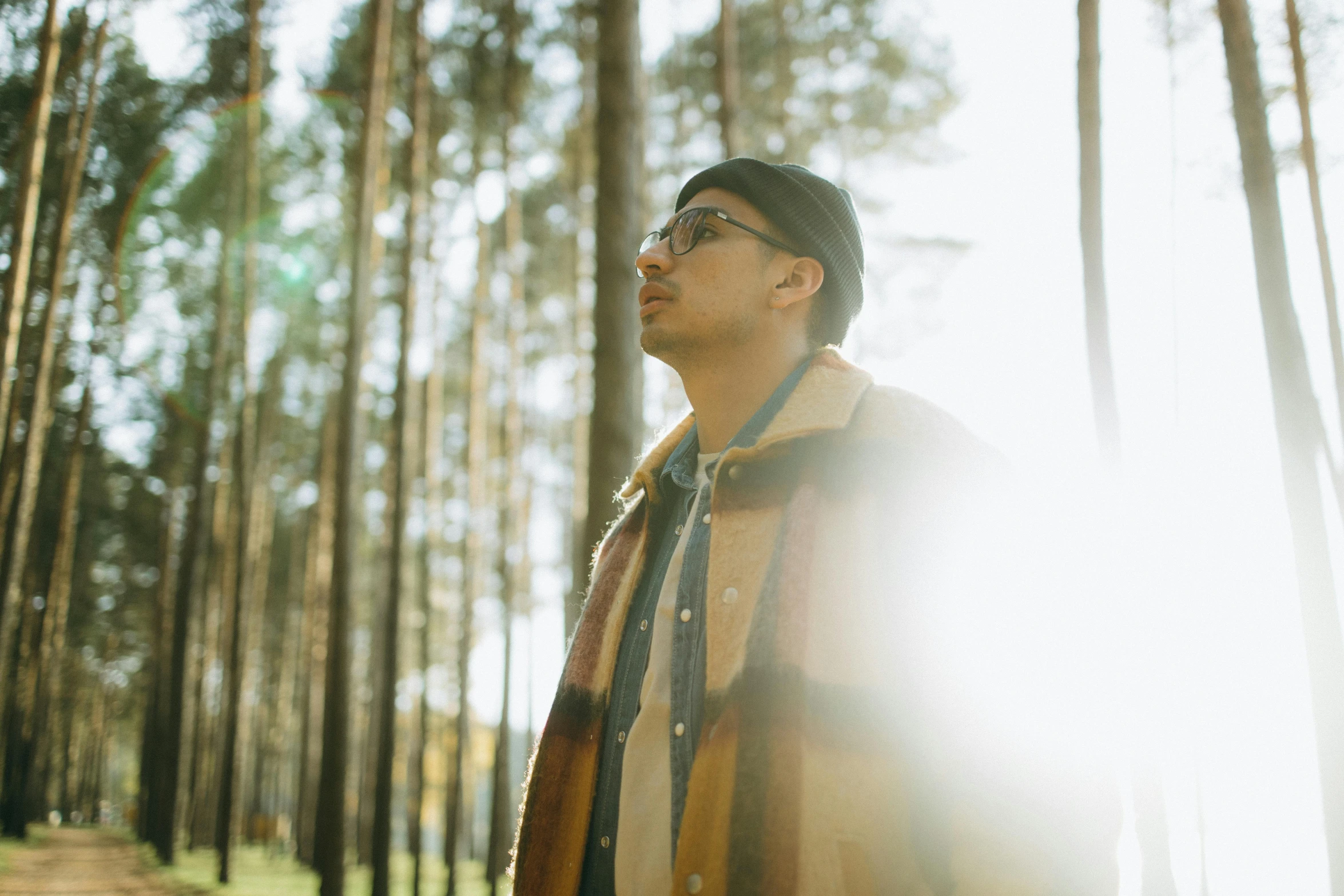 a man standing in the middle of a forest, an album cover, unsplash, man with glasses, golden light film grain, light skin, backlit shot girl in parka