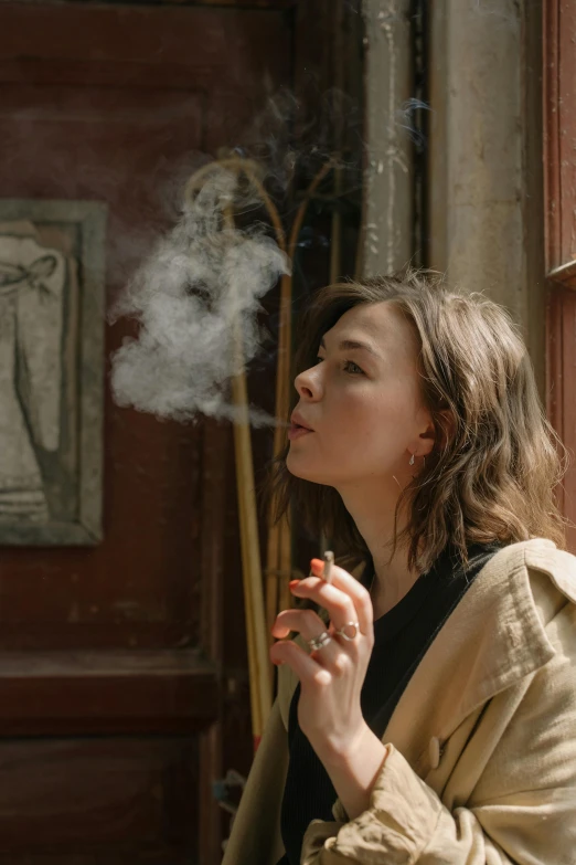 a woman smoking a cigarette in front of a door, trending on pexels, visual art, kiera knightly in repose, incense, ( ( theatrical ) ), haze over the shoulder shot